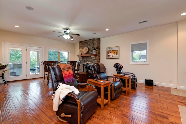 living room with ceiling fan, a stone fireplace, and light hardwood / wood-style floors