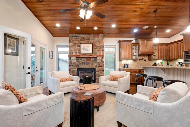 carpeted living room with ceiling fan, wood ceiling, vaulted ceiling, sink, and a fireplace