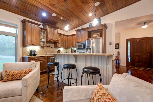 kitchen with light stone counters, a breakfast bar, vaulted ceiling, appliances with stainless steel finishes, and decorative light fixtures