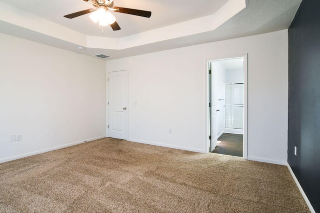 carpeted empty room featuring a raised ceiling and ceiling fan