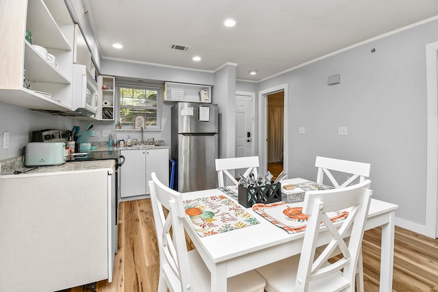 dining space featuring sink, light hardwood / wood-style flooring, and ornamental molding