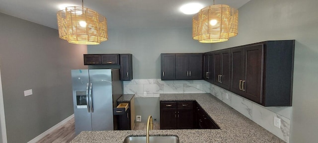 kitchen featuring pendant lighting, decorative backsplash, sink, and stainless steel refrigerator with ice dispenser