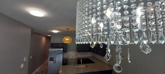 kitchen with kitchen peninsula, stainless steel fridge, light stone counters, and sink