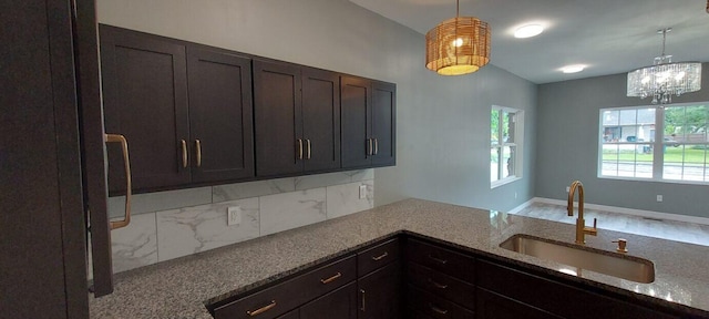 kitchen featuring light stone countertops, hardwood / wood-style flooring, sink, pendant lighting, and dark brown cabinets