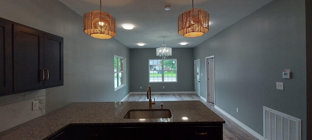 kitchen featuring light hardwood / wood-style flooring, dark stone counters, decorative light fixtures, and sink