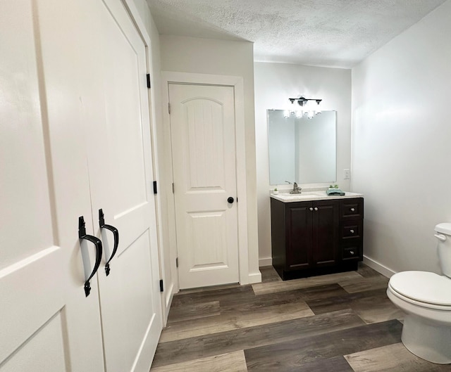 bathroom with toilet, vanity, wood-type flooring, and a textured ceiling