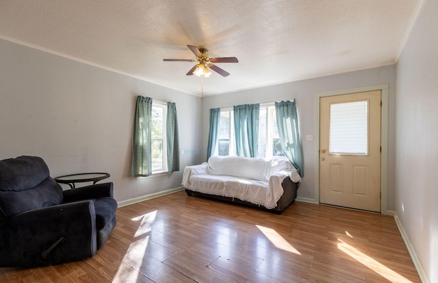 living room with ceiling fan, a textured ceiling, light wood-type flooring, and ornamental molding