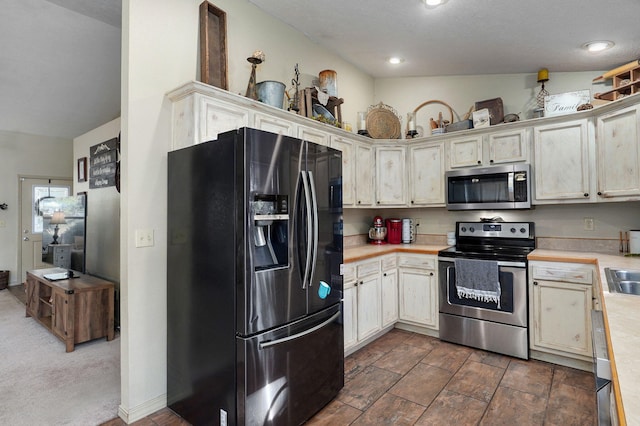 kitchen featuring stainless steel appliances, dark carpet, lofted ceiling, and sink