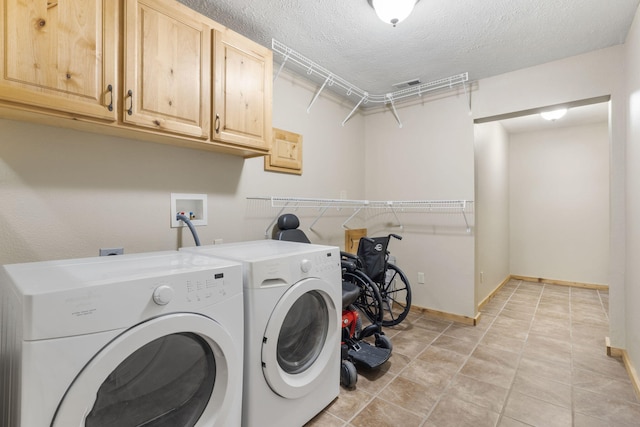 laundry area with a textured ceiling, separate washer and dryer, light tile patterned floors, and cabinets