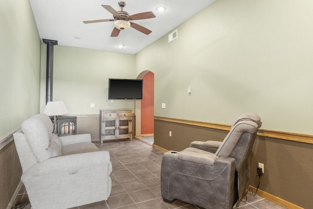 tiled living room featuring ceiling fan and a wood stove