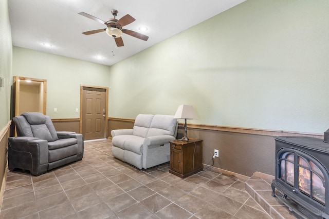 living area with ceiling fan, a wood stove, and tile patterned floors