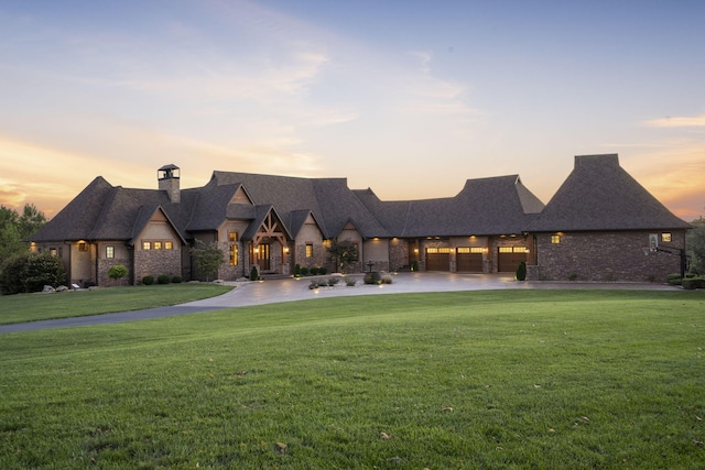 view of front of house with stone siding, a chimney, a garage, a lawn, and curved driveway