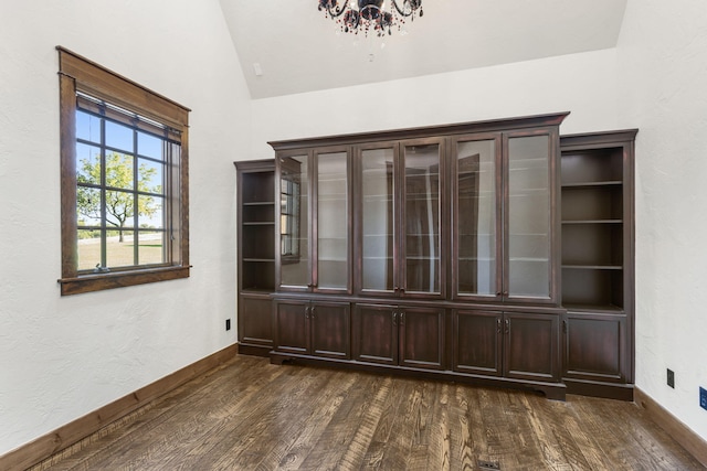 empty room featuring vaulted ceiling, dark wood-style flooring, a chandelier, and baseboards