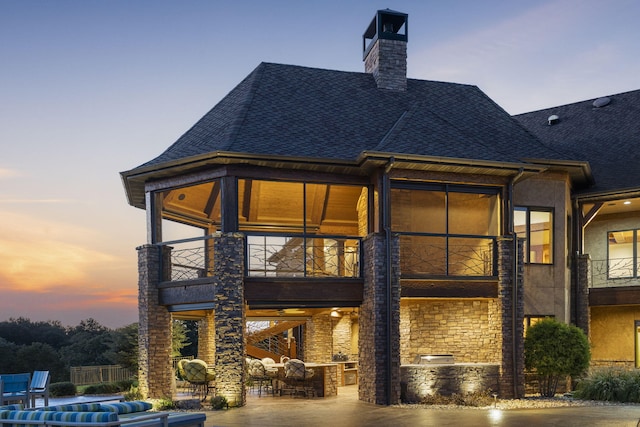 back of house featuring a patio area, a chimney, roof with shingles, and a balcony