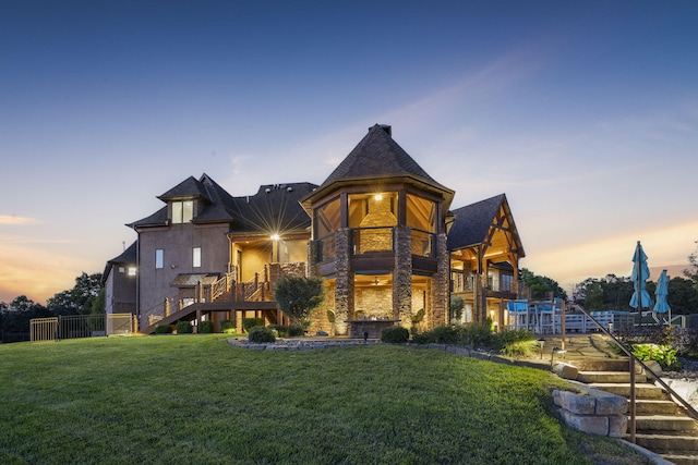 back of house at dusk with a yard, a balcony, stone siding, and stairway