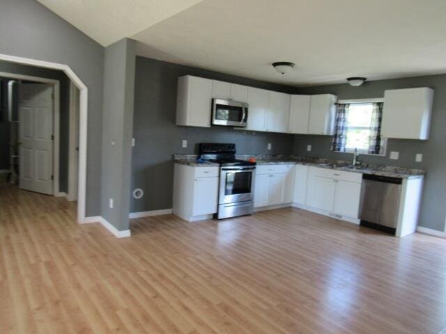 kitchen featuring light hardwood / wood-style flooring, stainless steel appliances, light stone countertops, and white cabinetry