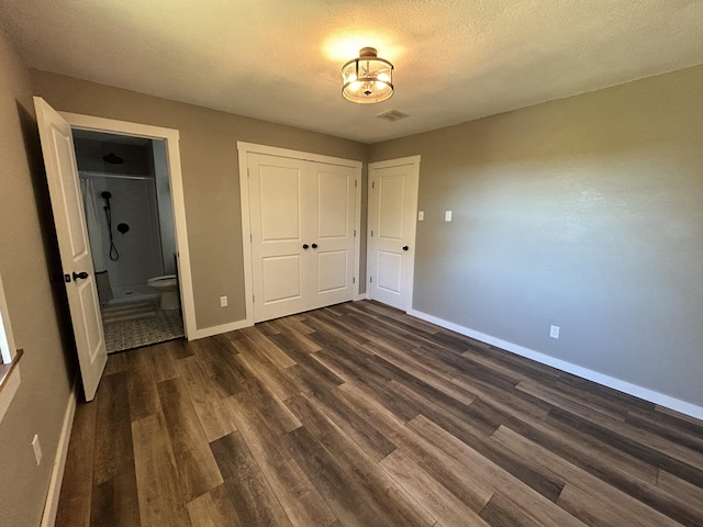 unfurnished bedroom with connected bathroom, a textured ceiling, and dark hardwood / wood-style flooring