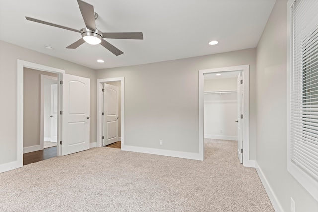 unfurnished bedroom featuring light carpet, a closet, a spacious closet, and ceiling fan