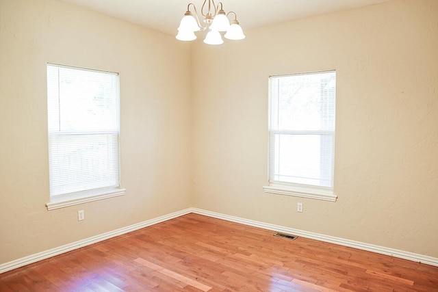 spare room with wood-type flooring, plenty of natural light, and a chandelier