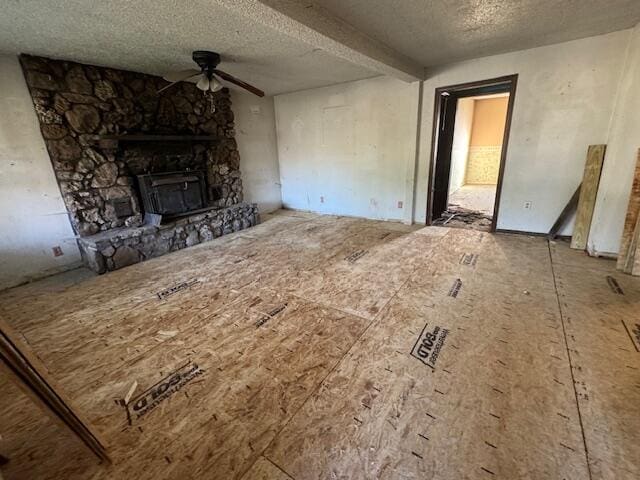 unfurnished living room with a stone fireplace, a textured ceiling, and ceiling fan