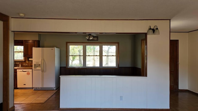 kitchen with a textured ceiling, wooden walls, white appliances, and decorative backsplash