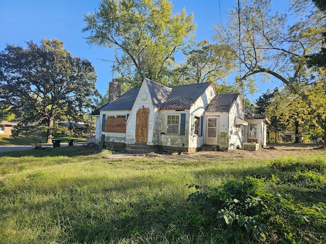 view of front facade with entry steps, metal roof, central air condition unit, a chimney, and a front yard