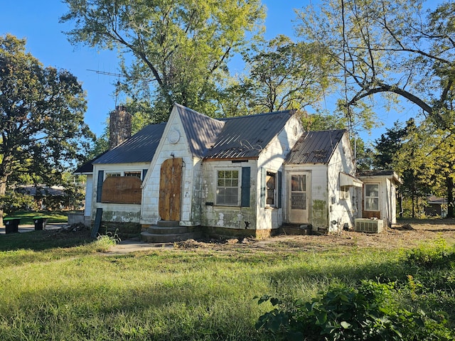 view of front of house with entry steps, central AC unit, a chimney, metal roof, and a front yard