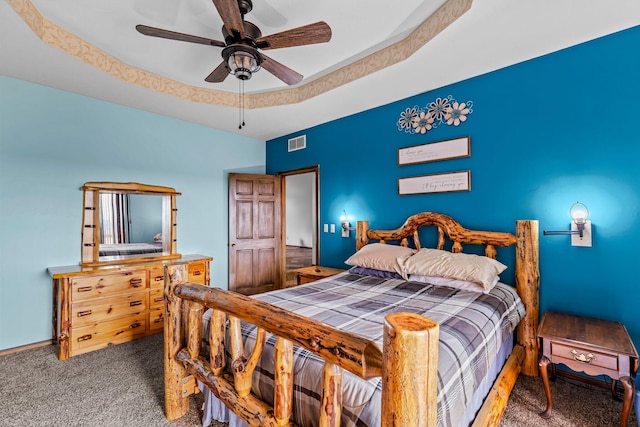 bedroom with dark colored carpet, ceiling fan, and a raised ceiling