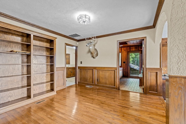 unfurnished dining area featuring ornamental molding, a textured ceiling, wooden walls, and light hardwood / wood-style floors