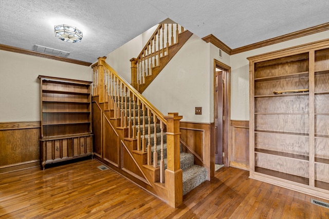 stairway with ornamental molding, hardwood / wood-style floors, and a textured ceiling