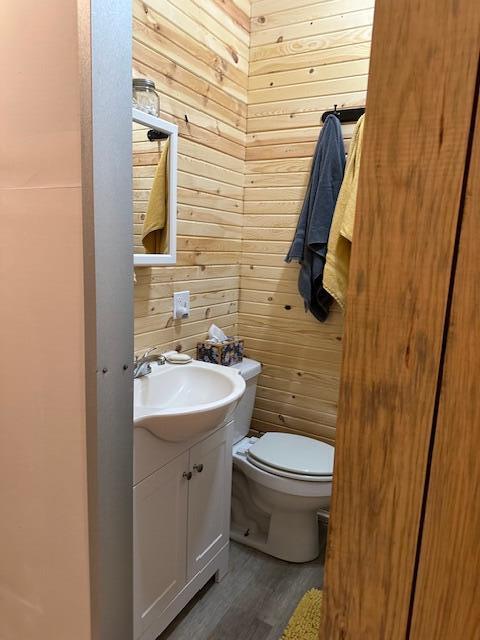 bathroom with vanity, hardwood / wood-style floors, toilet, and wooden walls