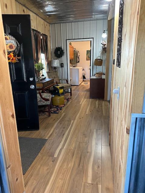 hall with washing machine and dryer, hardwood / wood-style flooring, and wood walls