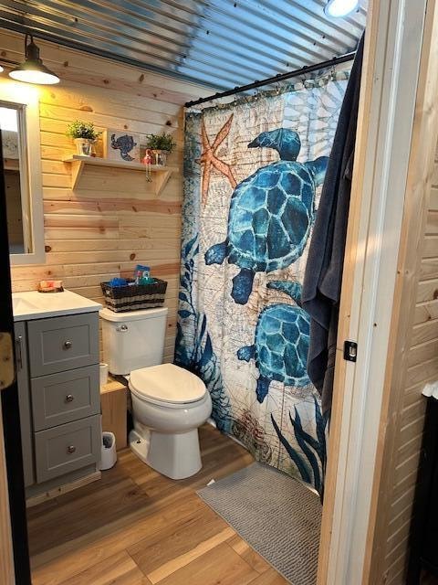 bathroom featuring curtained shower, hardwood / wood-style floors, toilet, wooden walls, and vanity