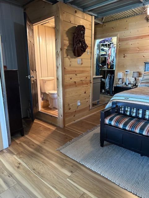 bedroom featuring ensuite bathroom, wood-type flooring, and wood walls