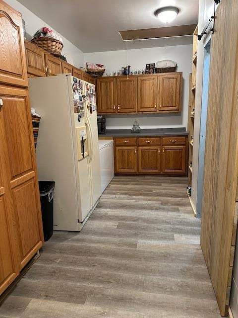 kitchen featuring washer / clothes dryer, hardwood / wood-style floors, a barn door, and white refrigerator with ice dispenser