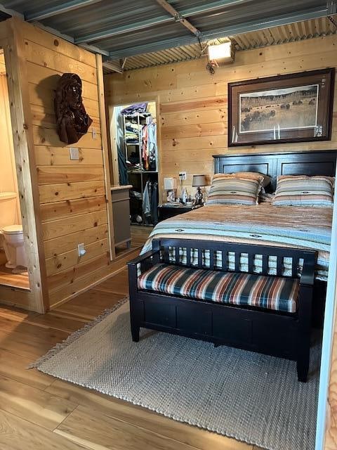 bedroom with beamed ceiling, connected bathroom, hardwood / wood-style floors, and wood walls