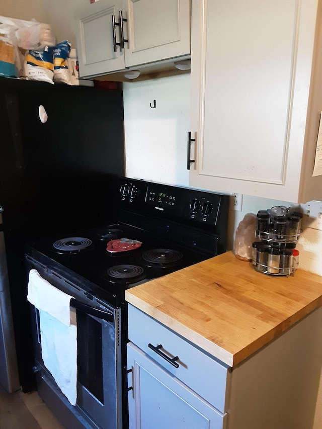 kitchen with butcher block countertops, white cabinetry, and black range with electric cooktop