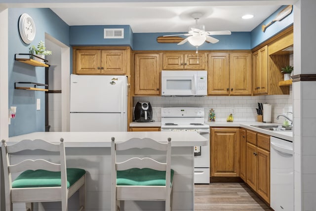 kitchen with a breakfast bar area, light hardwood / wood-style flooring, backsplash, sink, and white appliances