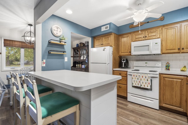 kitchen featuring white appliances, backsplash, a kitchen breakfast bar, pendant lighting, and light hardwood / wood-style flooring