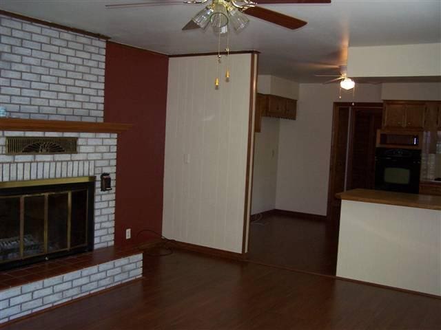 unfurnished living room featuring dark wood-type flooring, ceiling fan, and a brick fireplace