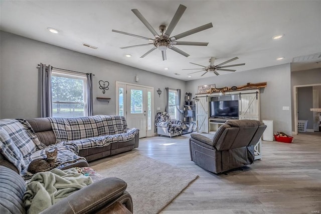 living room with a wealth of natural light, a barn door, light hardwood / wood-style floors, and ceiling fan