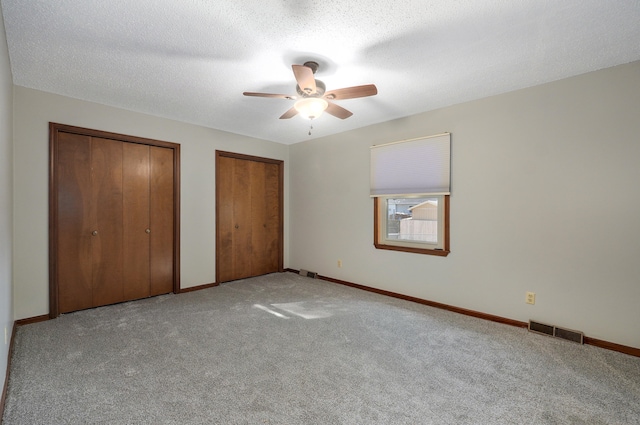 unfurnished bedroom featuring ceiling fan, multiple closets, and light colored carpet