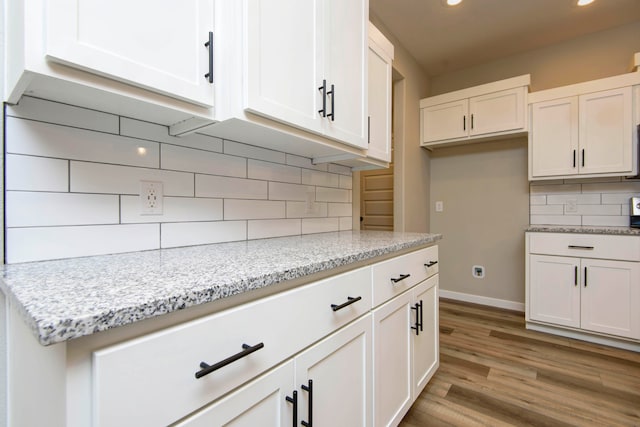 kitchen with white cabinets, light stone countertops, backsplash, and light hardwood / wood-style flooring