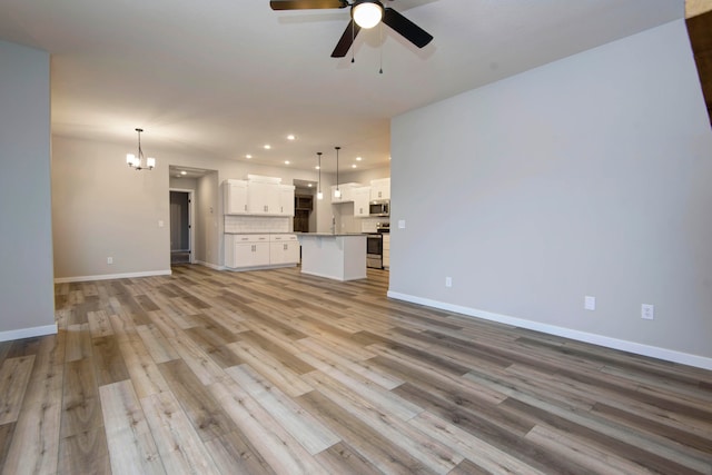 unfurnished living room with ceiling fan with notable chandelier and light hardwood / wood-style flooring