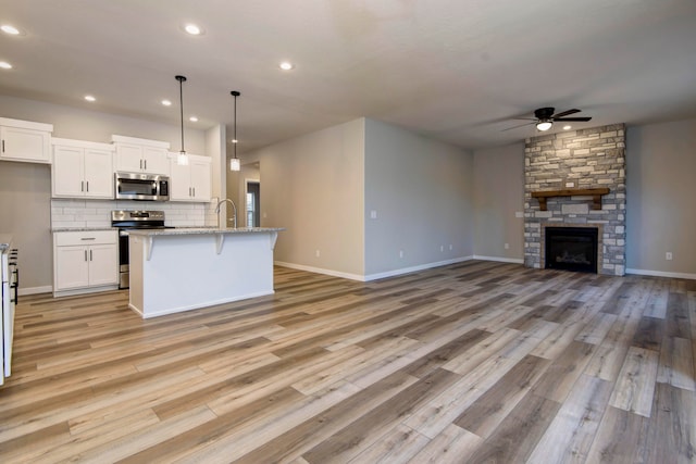 kitchen featuring hanging light fixtures, stainless steel appliances, a stone fireplace, a center island with sink, and white cabinets