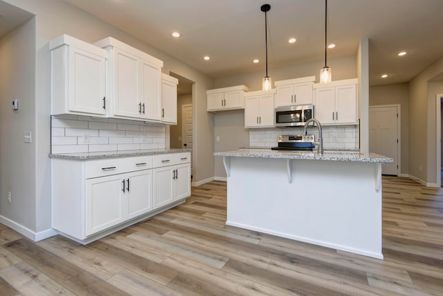 kitchen featuring pendant lighting, white cabinets, light stone countertops, an island with sink, and appliances with stainless steel finishes