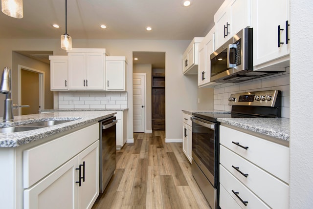 kitchen featuring light wood-type flooring, white cabinetry, light stone counters, and appliances with stainless steel finishes