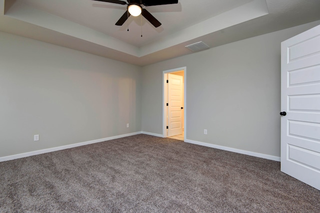 empty room featuring a raised ceiling, ceiling fan, and carpet