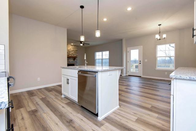 kitchen featuring stainless steel dishwasher, an island with sink, light hardwood / wood-style floors, white cabinets, and ceiling fan with notable chandelier