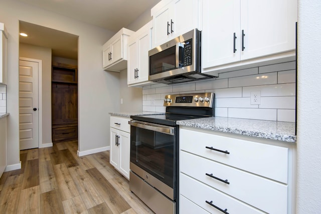 kitchen with light stone countertops, light hardwood / wood-style flooring, backsplash, white cabinets, and appliances with stainless steel finishes